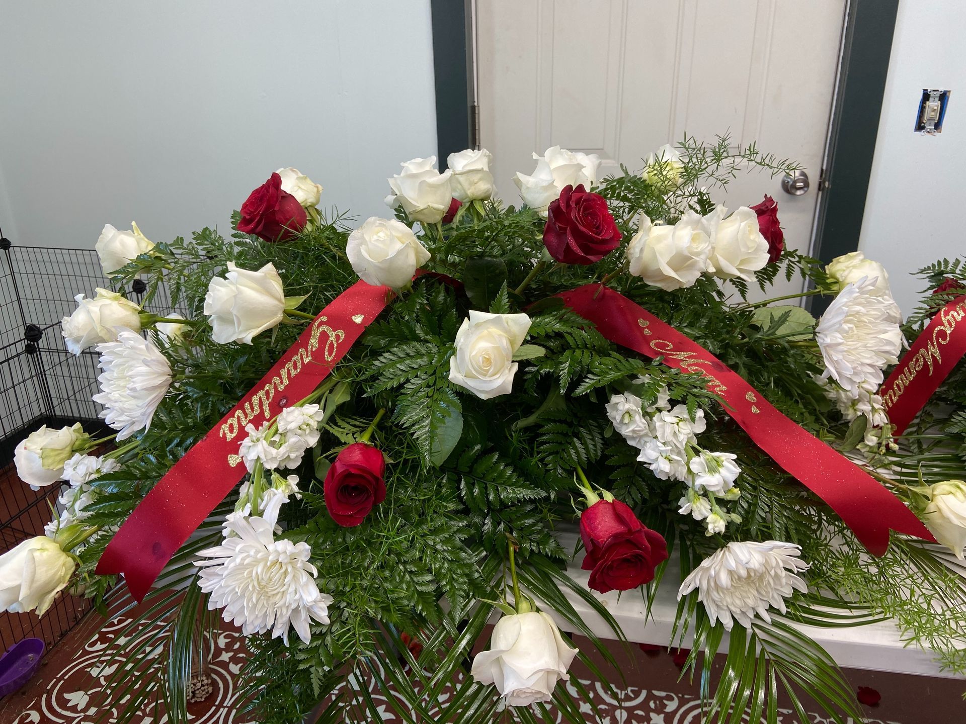 Floral funeral arrangement with red, white, and green flowers and red ribbons on a casket