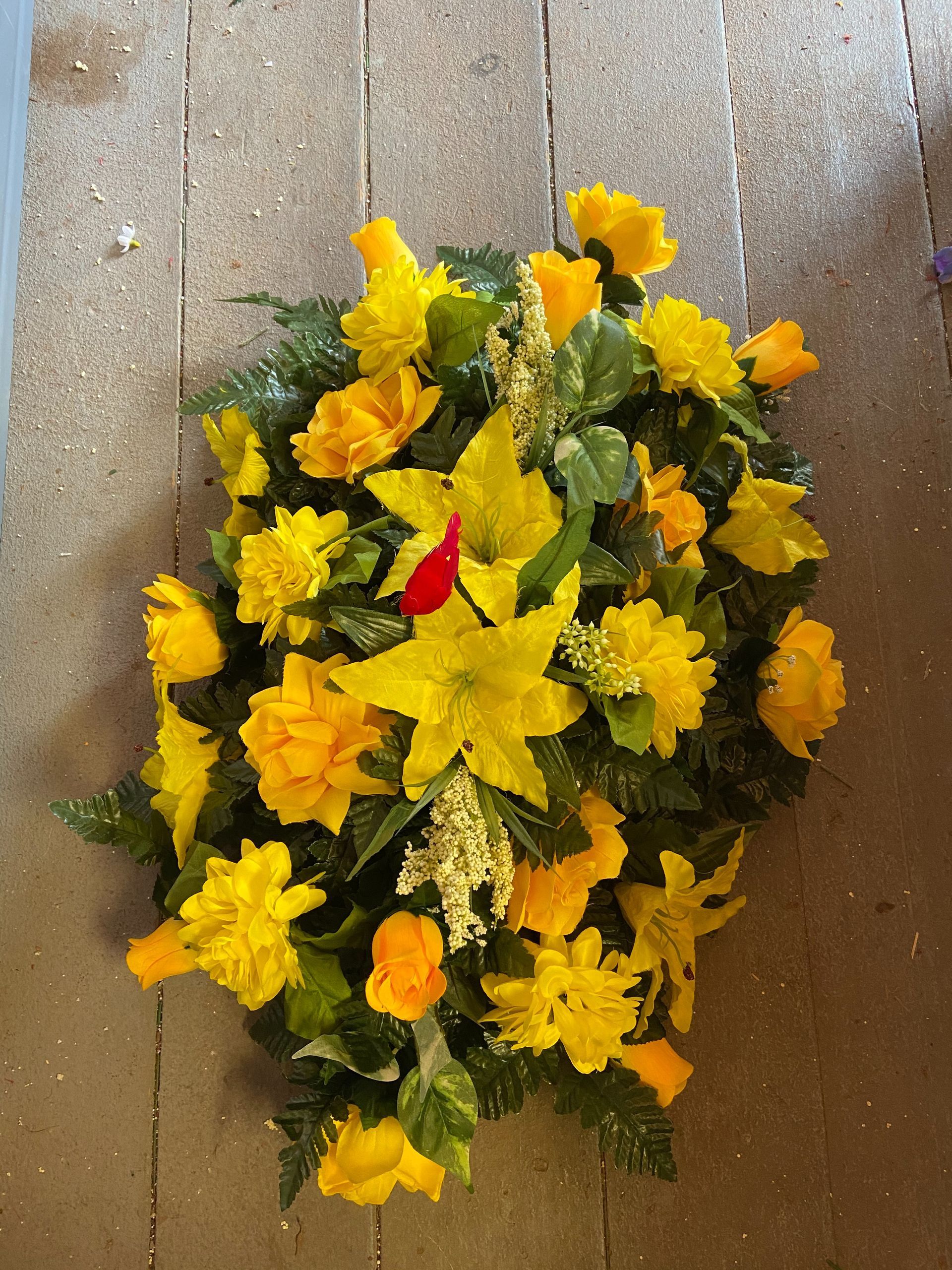 Yellow floral arrangement with green leaves and a single red accent on a wooden surface