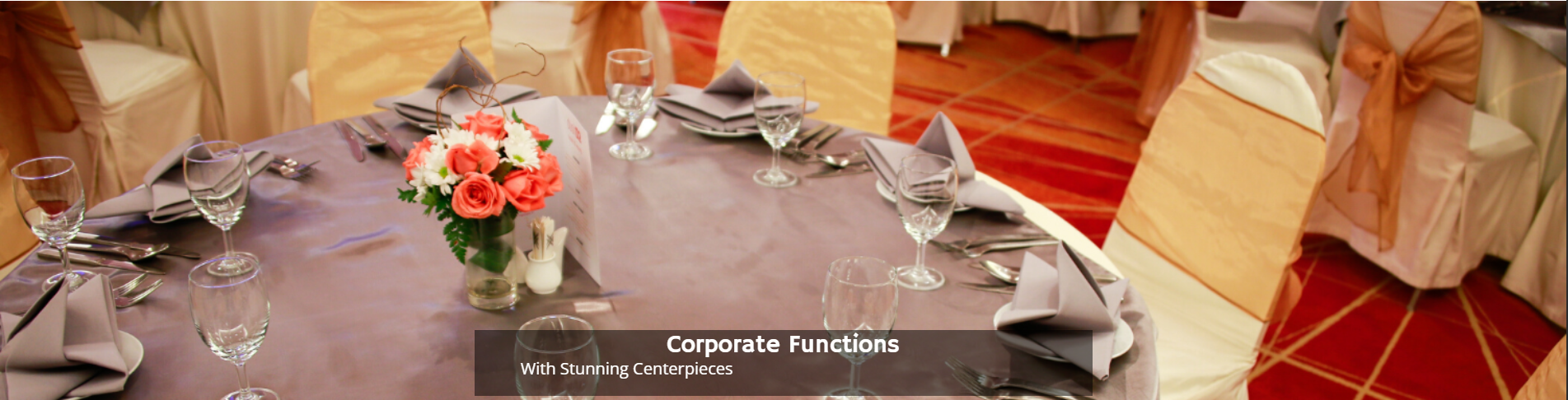 Elegant banquet table with dark tablecloth, floral centerpiece, and gold chair bows in a decorated hall