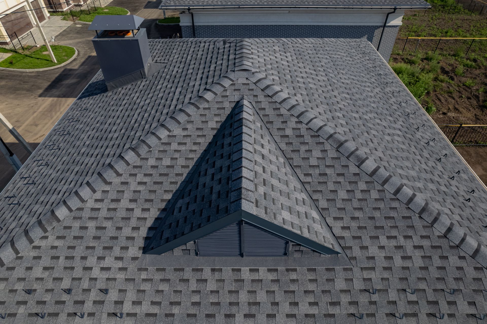 Aerial view of a gray shingled roof with a central dormer and rooftop vent