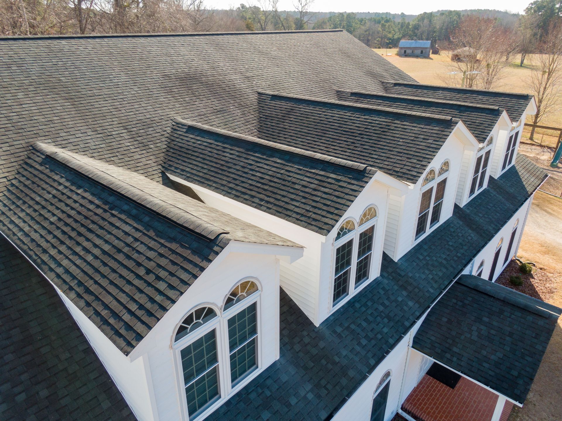 Aerial view of a house roof with three dormers and white trim on a wooded property