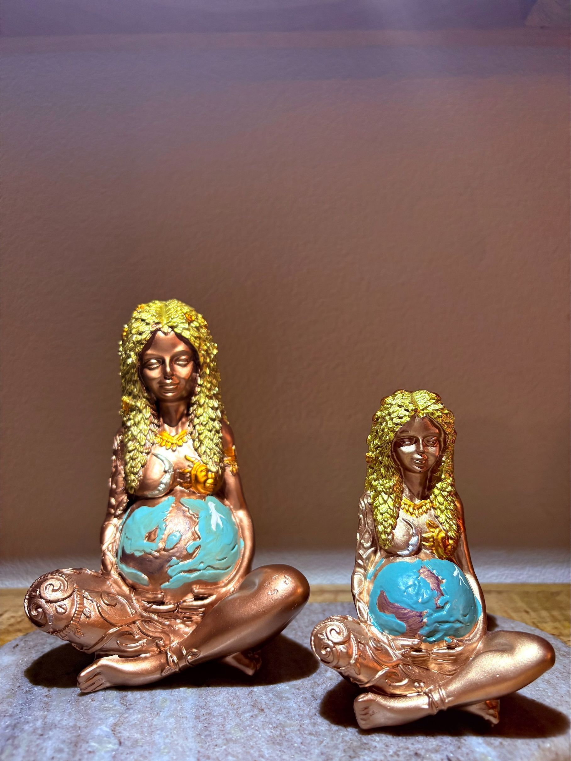 Gouden beeld van een zittende vrouw die een blauwe wereldbol vasthoudt. Ernaast staat een kaars in een groene houder.