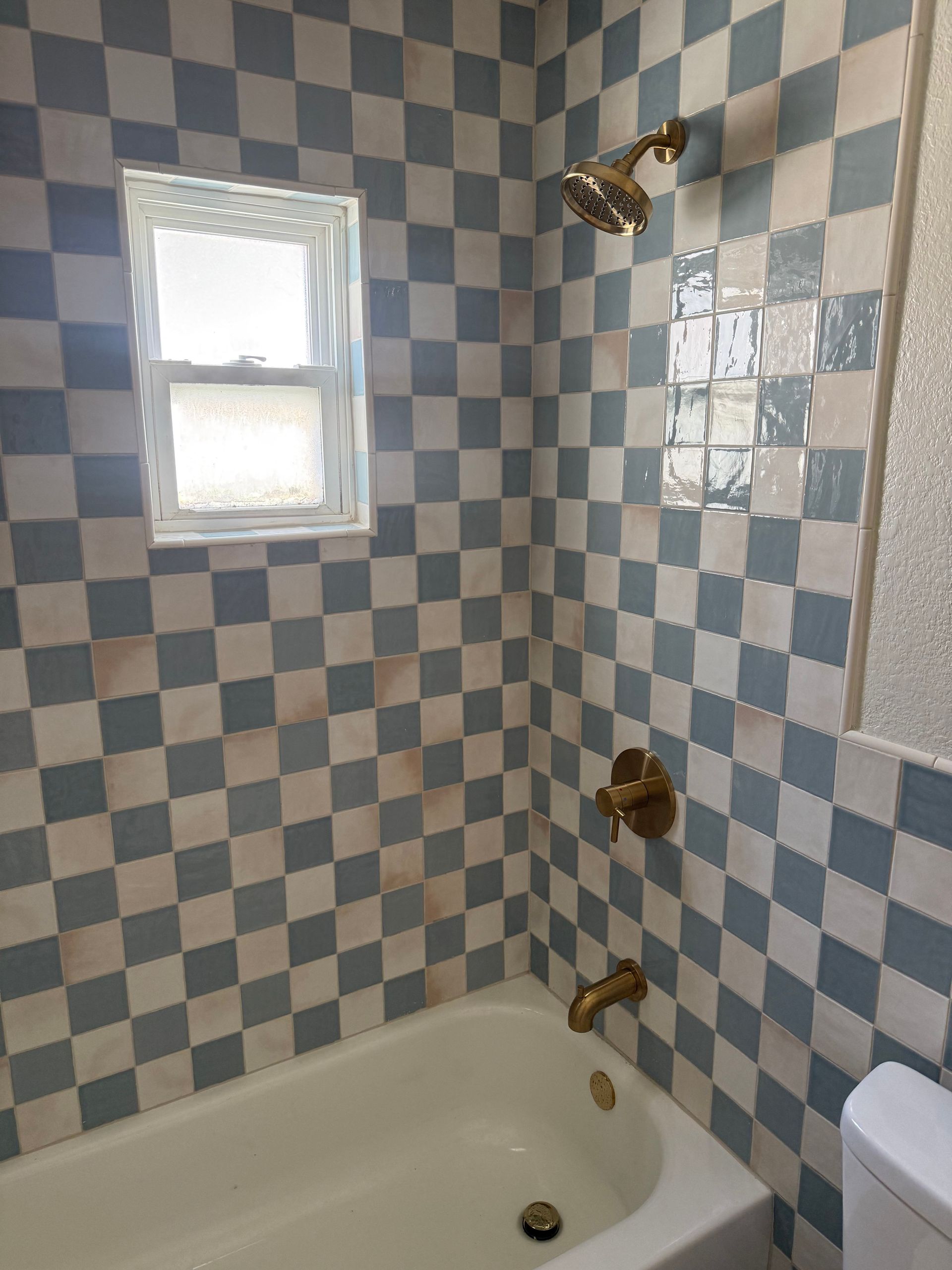 Blue-and-white tiled bathroom with a bathtub, window, and shower fixtures