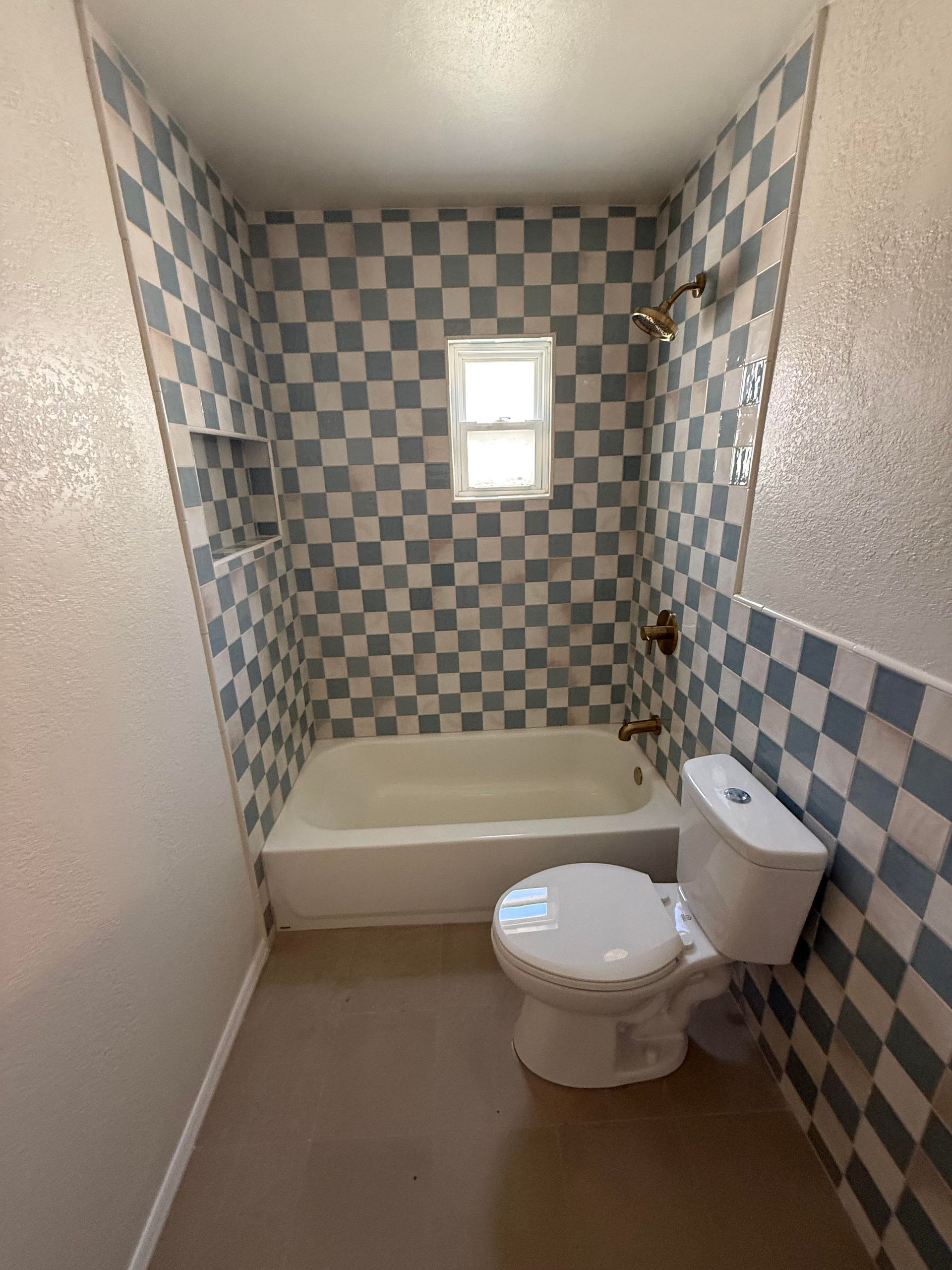 Small bathroom with checkerboard tile, bathtub, toilet, and a small window.