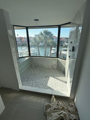 Indoor balcony alcove with tiled floor and large windows overlooking water and buildings, with laundry on the floor