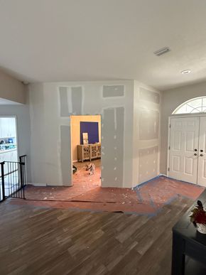Partially renovated living room with exposed drywall and a doorway to a room with boxes