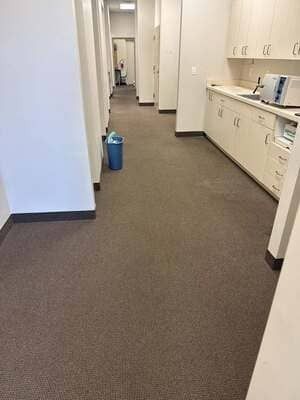 Office hallway with beige carpet, white cabinets, and a blue trash bin.
