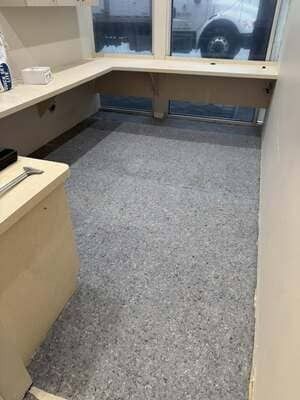 Empty office cubicle with gray carpet, beige desk surfaces, and a window view at the back.
