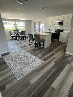 Open-concept kitchen and dining area with gray flooring, white cabinets, and a dining table by the windows