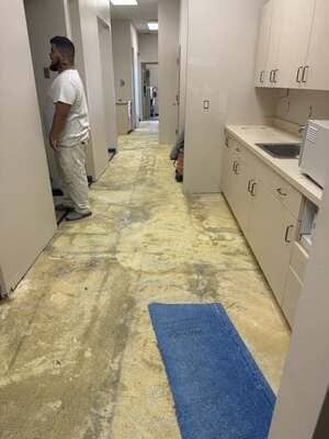 Narrow clinic hallway with cabinets, a blue floor mat, and a person standing near the wall