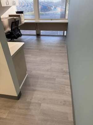 Empty office hallway with gray flooring, desks, and large windows at the end.