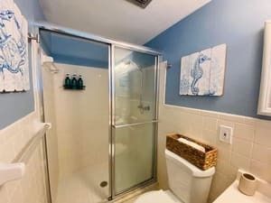 Bathroom with glass shower, white walls, blue ceiling, towel bars, and a wicker hamper.