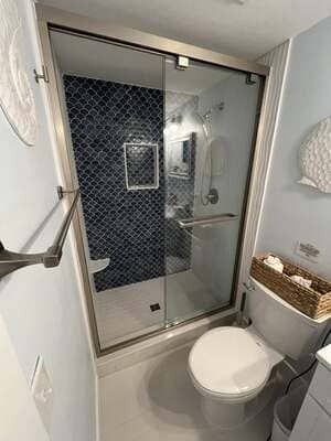 Small bathroom with glass shower, white toilet, and dark tiled shower wall.