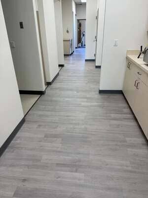 Empty hallway with gray wood flooring, white walls, and cabinets along the right side.