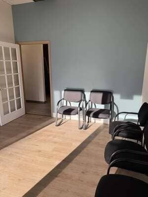 Empty room with chairs along the wall, a glass door on the left, and sunlight across the floor.