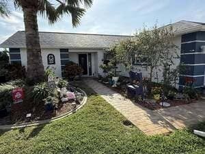 Single-story house with a landscaped front yard, stone walkway, and palm trees