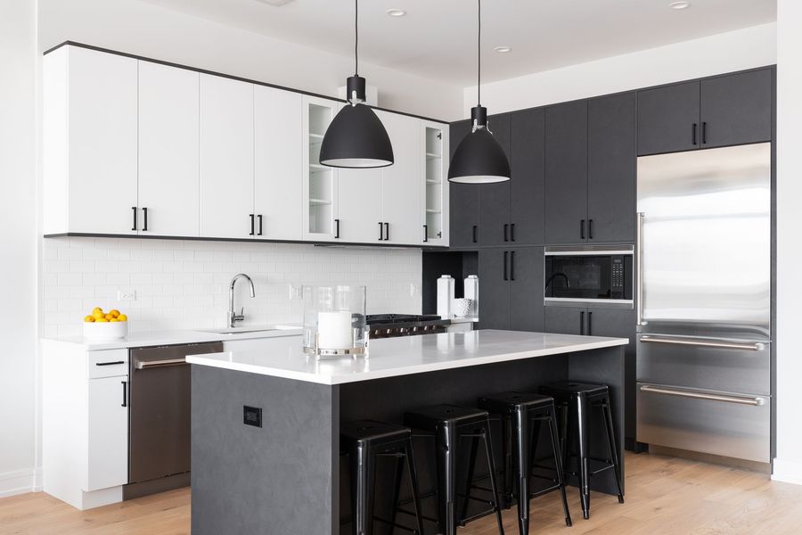 Modern kitchen with white and dark gray cabinets, stainless steel appliances, and a black island with bar stools
