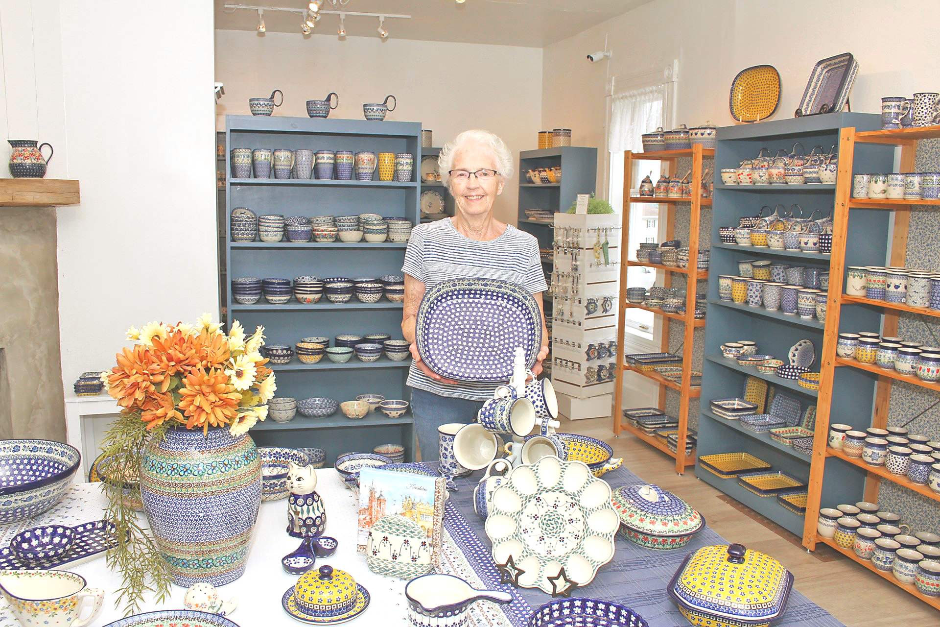 Woman in a pottery shop, holding a purple and blue basket; displays of blue pottery on shelves and tables.