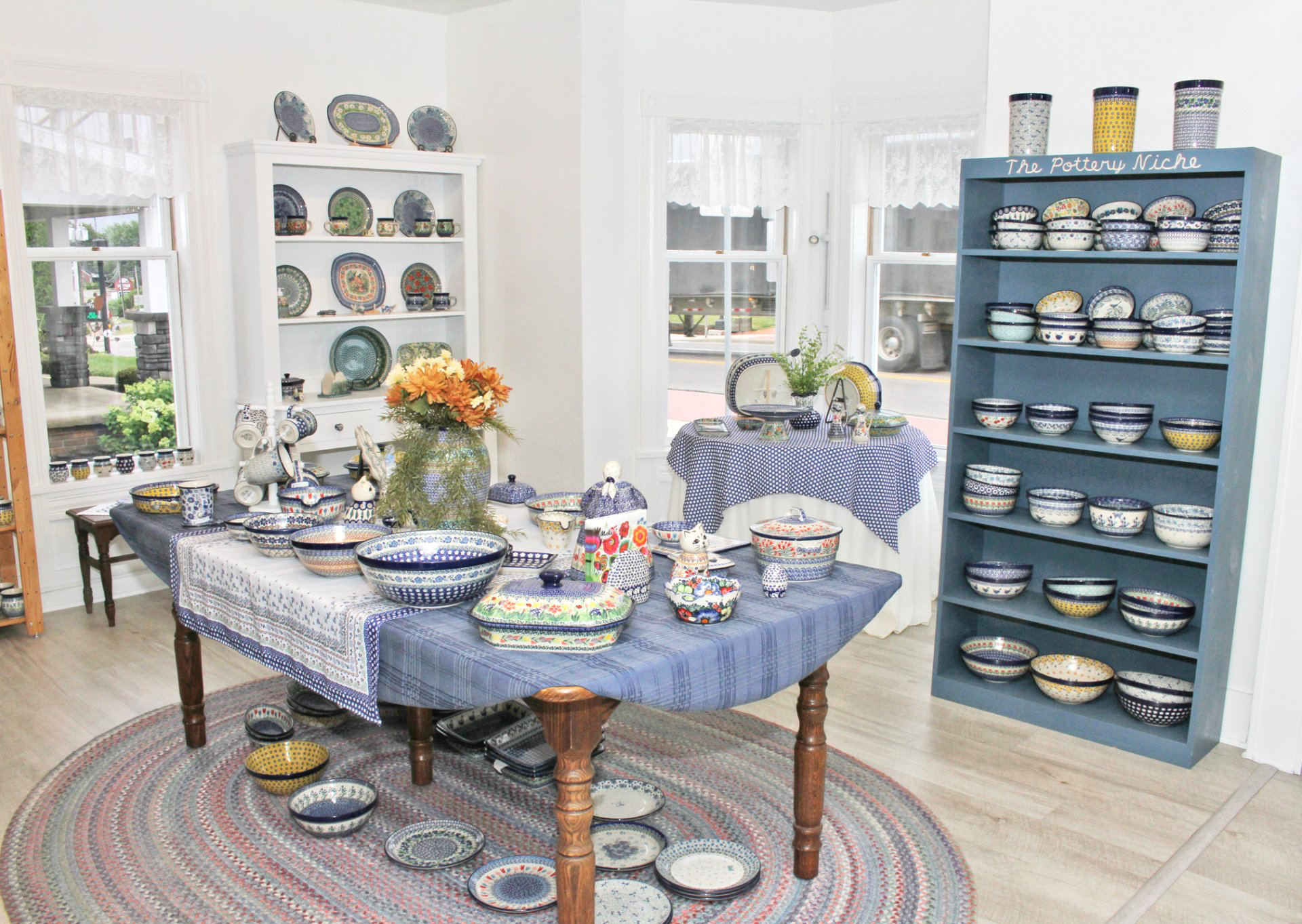 Shop interior with pottery, tables, shelves, and a rug. Mostly blue and white.