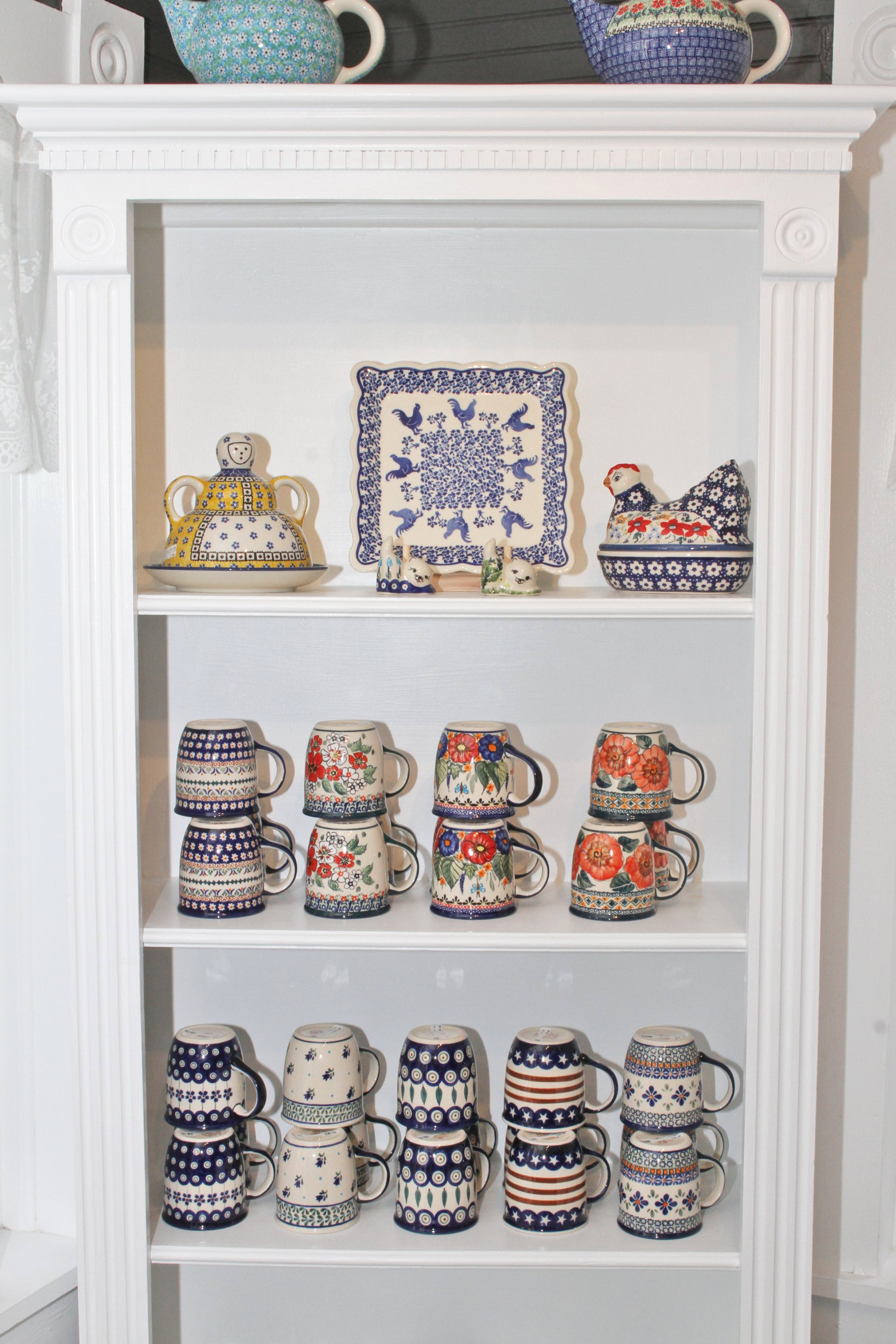 White shelving unit displays patterned ceramic teacups and teapots in various styles.