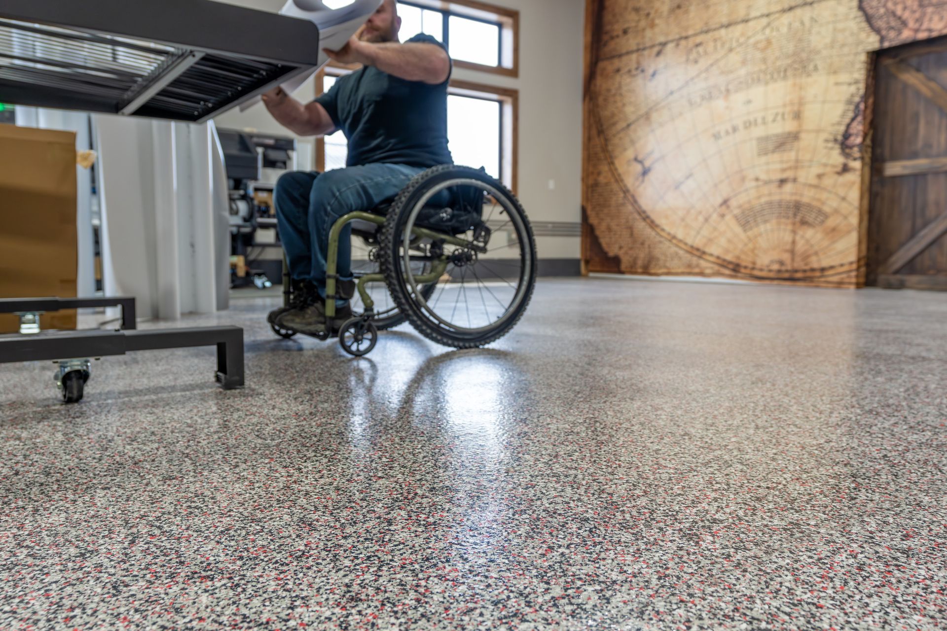 Man in a wheelchair working at a desk in a bright workshop with a speckled floor