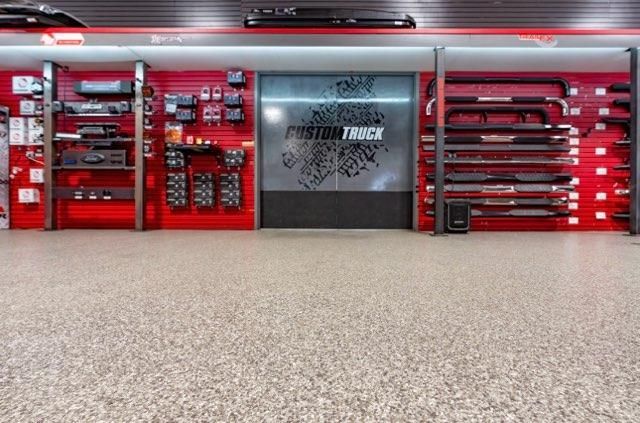 Red tool cabinets and equipment wall in a garage with a speckled floor, centered on a gray metal door