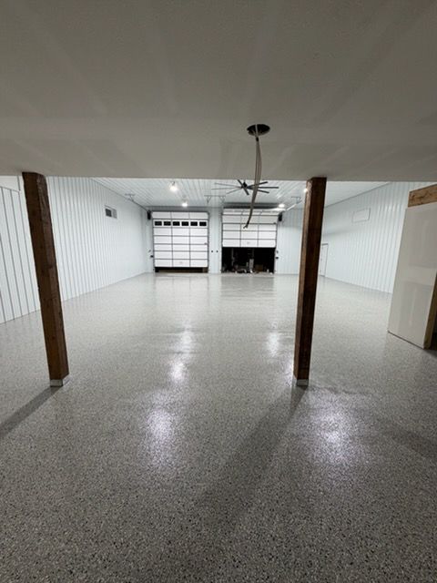 Empty garage with speckled floor, white walls, wooden posts, and overhead door at the back.