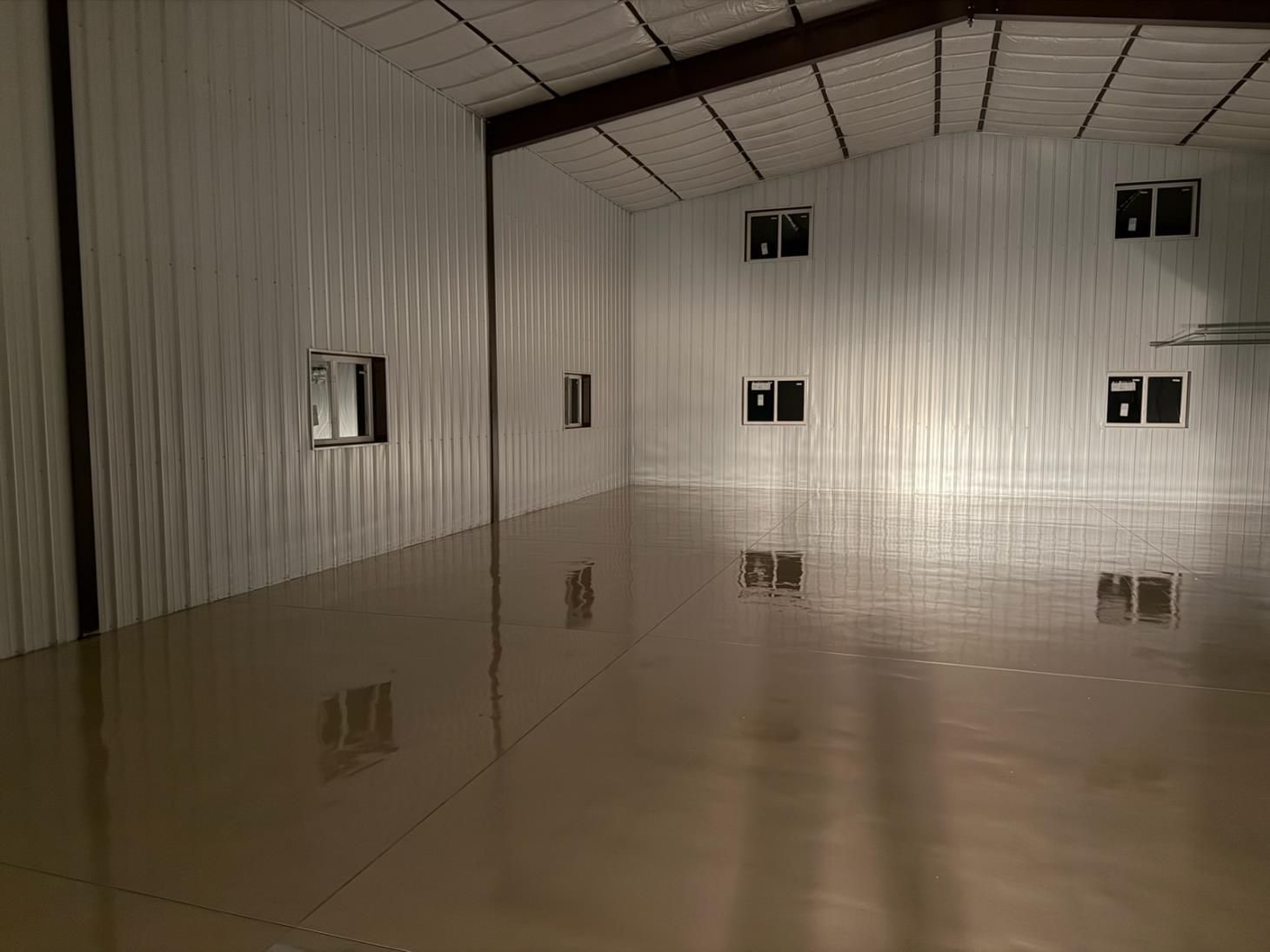 Empty industrial room with corrugated metal walls, small windows, and a glossy reflective floor.