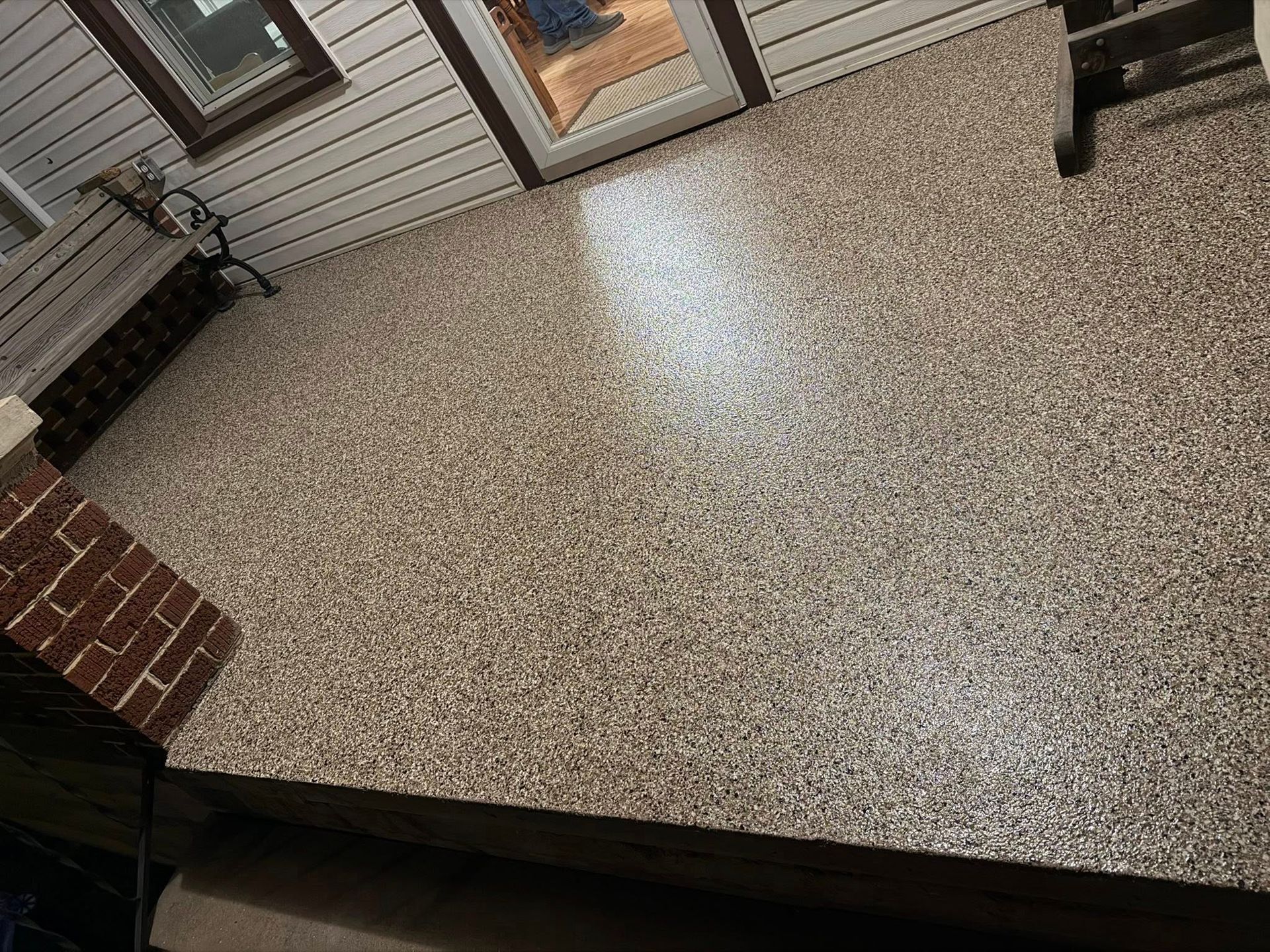 Speckled stone patio floor beside a brick wall and house siding with sliding glass doors.