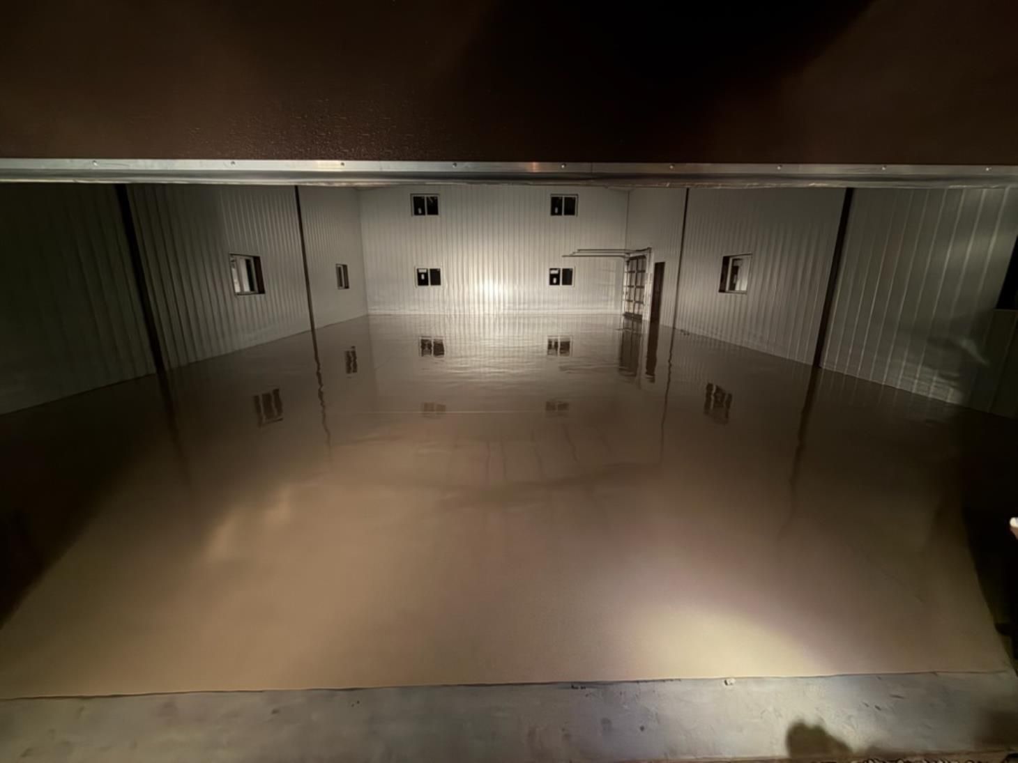 Empty indoor storage unit with metal walls and a glossy floor reflecting the doors.