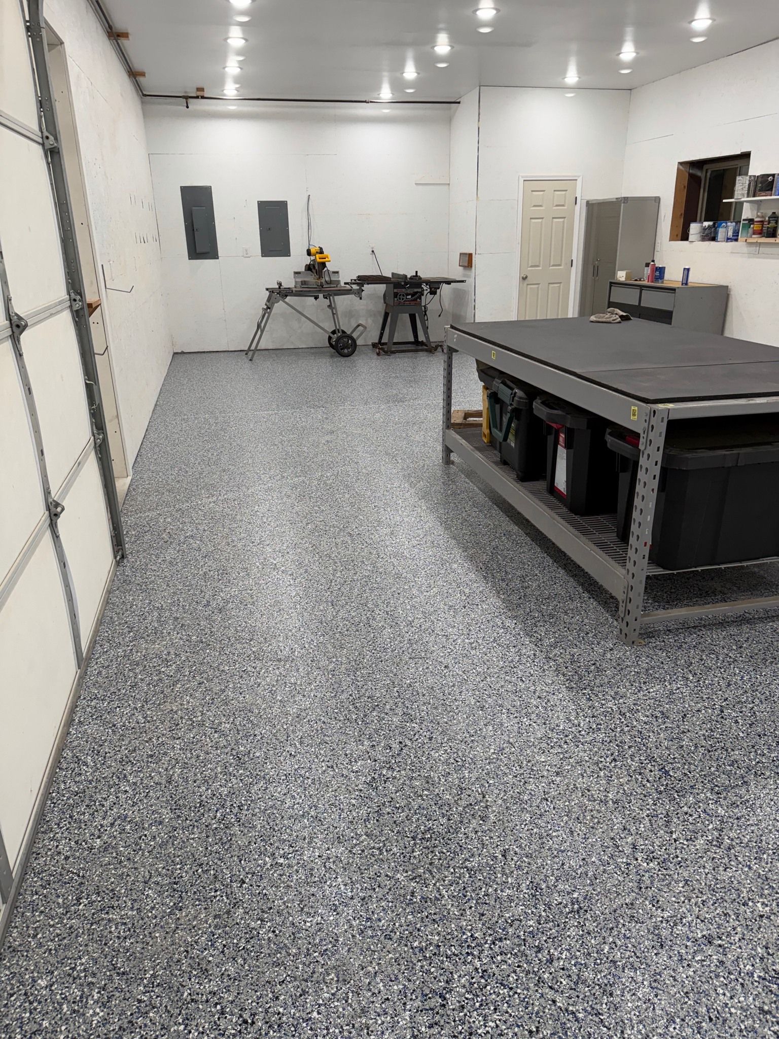 Spacious workshop with speckled floor, workbench, overhead lights, and storage cabinets.