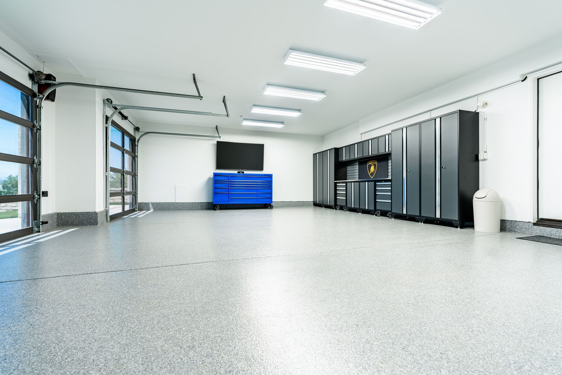 Empty modern garage with gray floor, white walls, overhead lights, and blue tool cabinets.