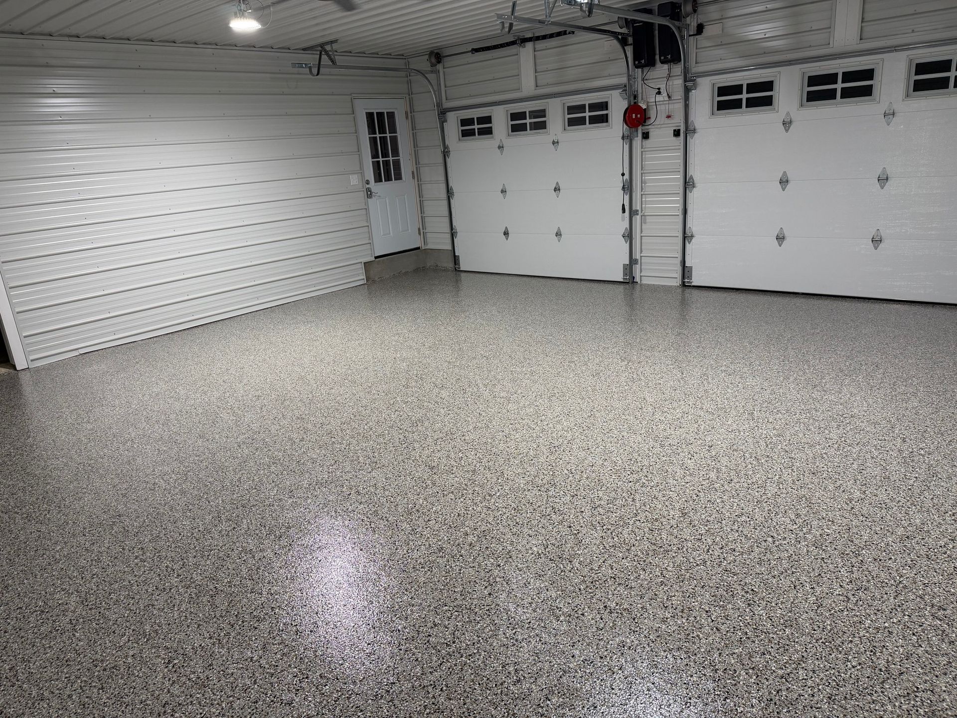 Empty garage with white walls, two garage doors, and speckled epoxy floor.