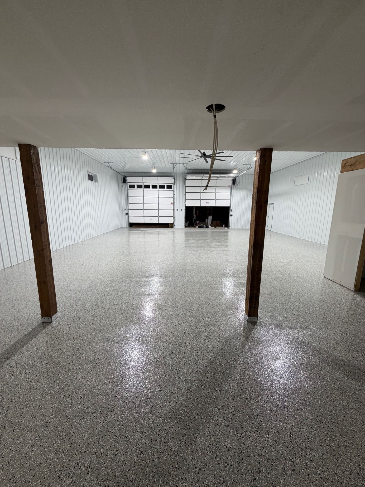 Empty white room with speckled floor, exposed wooden columns, and bright window at the back