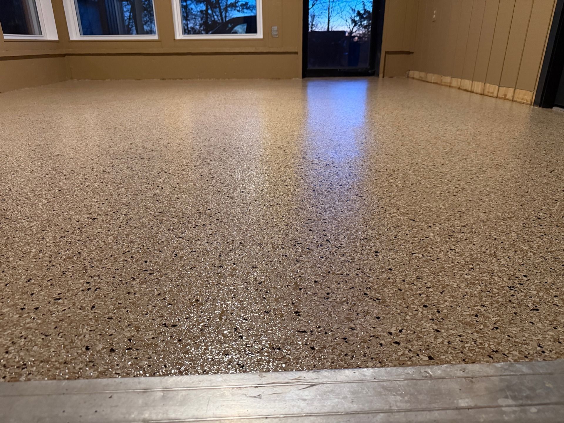 Tan speckled epoxy floor in an empty room with windows and a glass door.