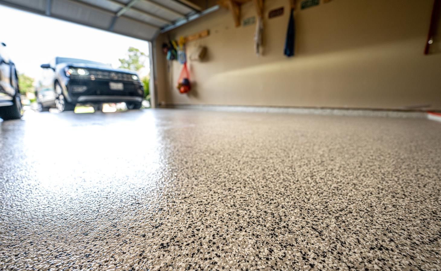 Low-angle view of a garage floor with a parked car in the background and tools on the wall.