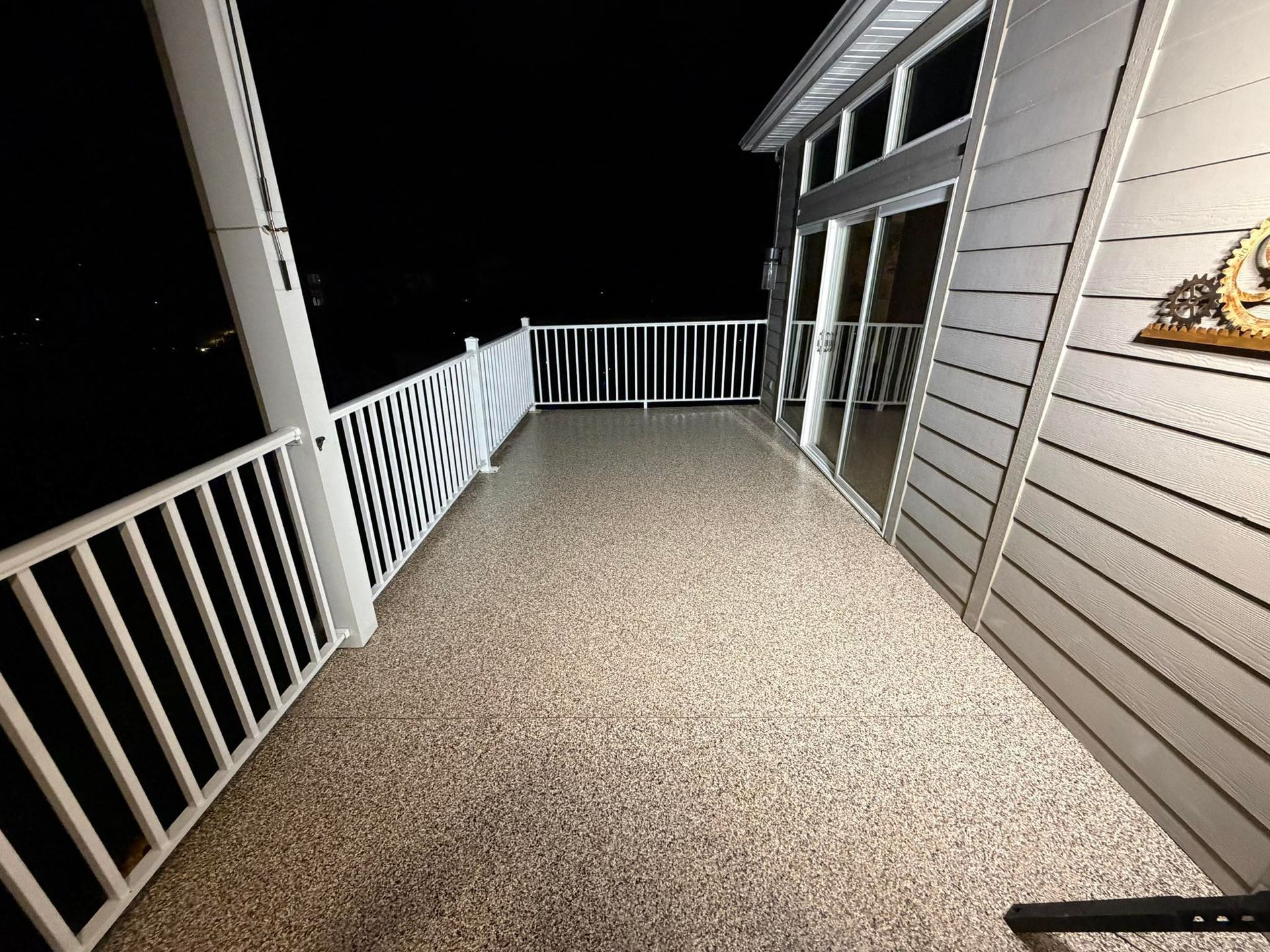 Nighttime view of a house deck with white railings and sliding glass doors along the side of the home