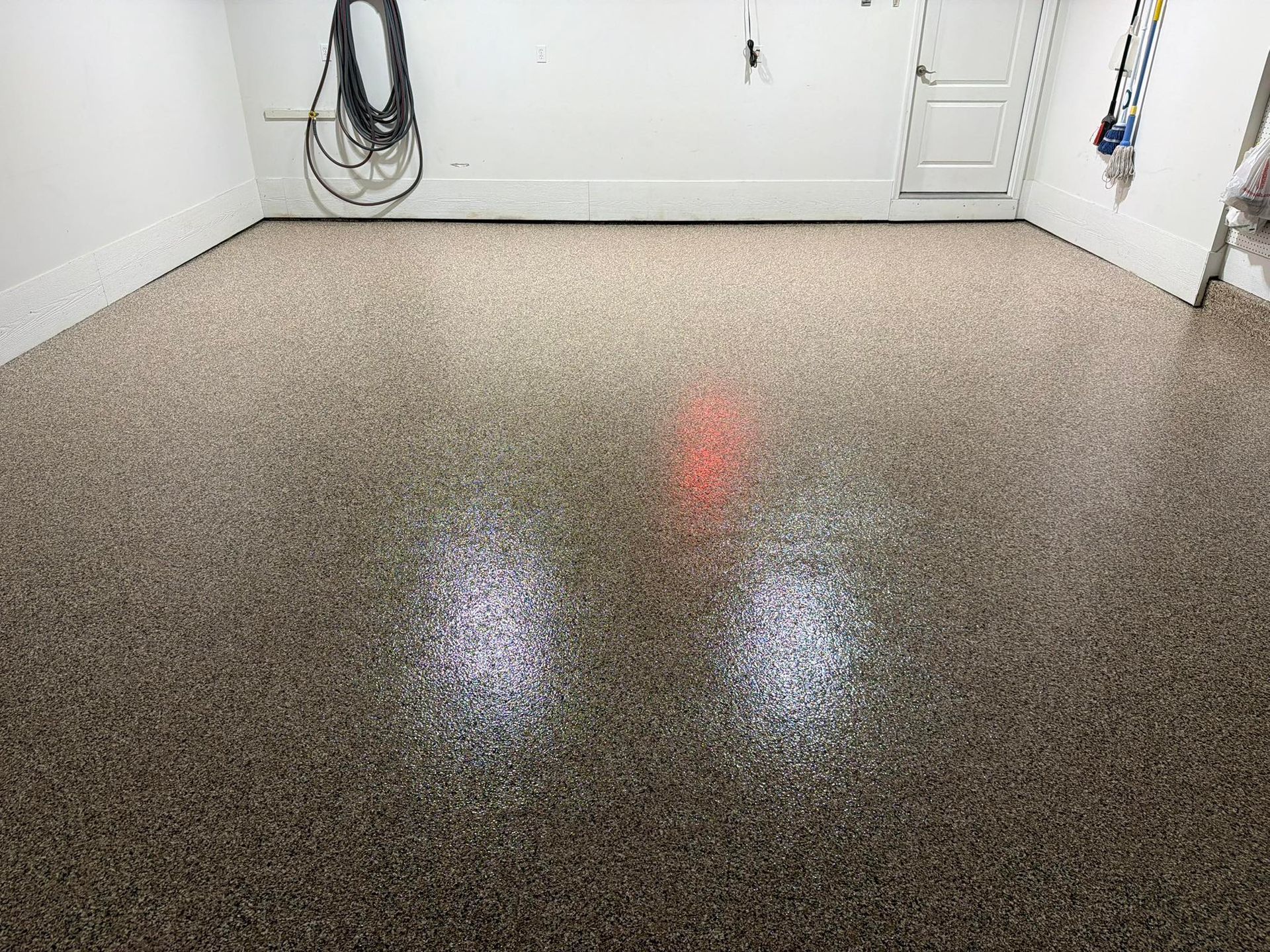 Empty speckled garage floor with white walls and hanging hoses in the back corner