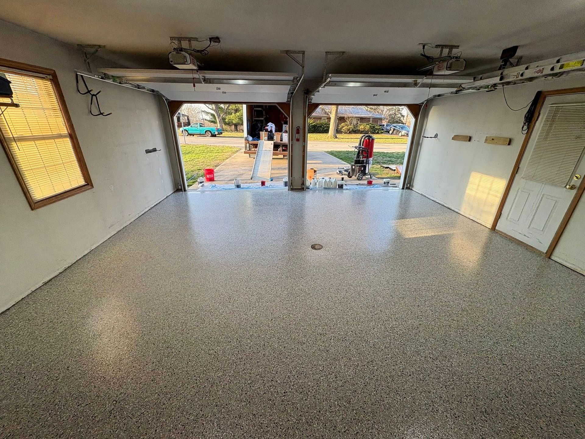 Empty garage with speckled floor, open door, and two people visible outside.