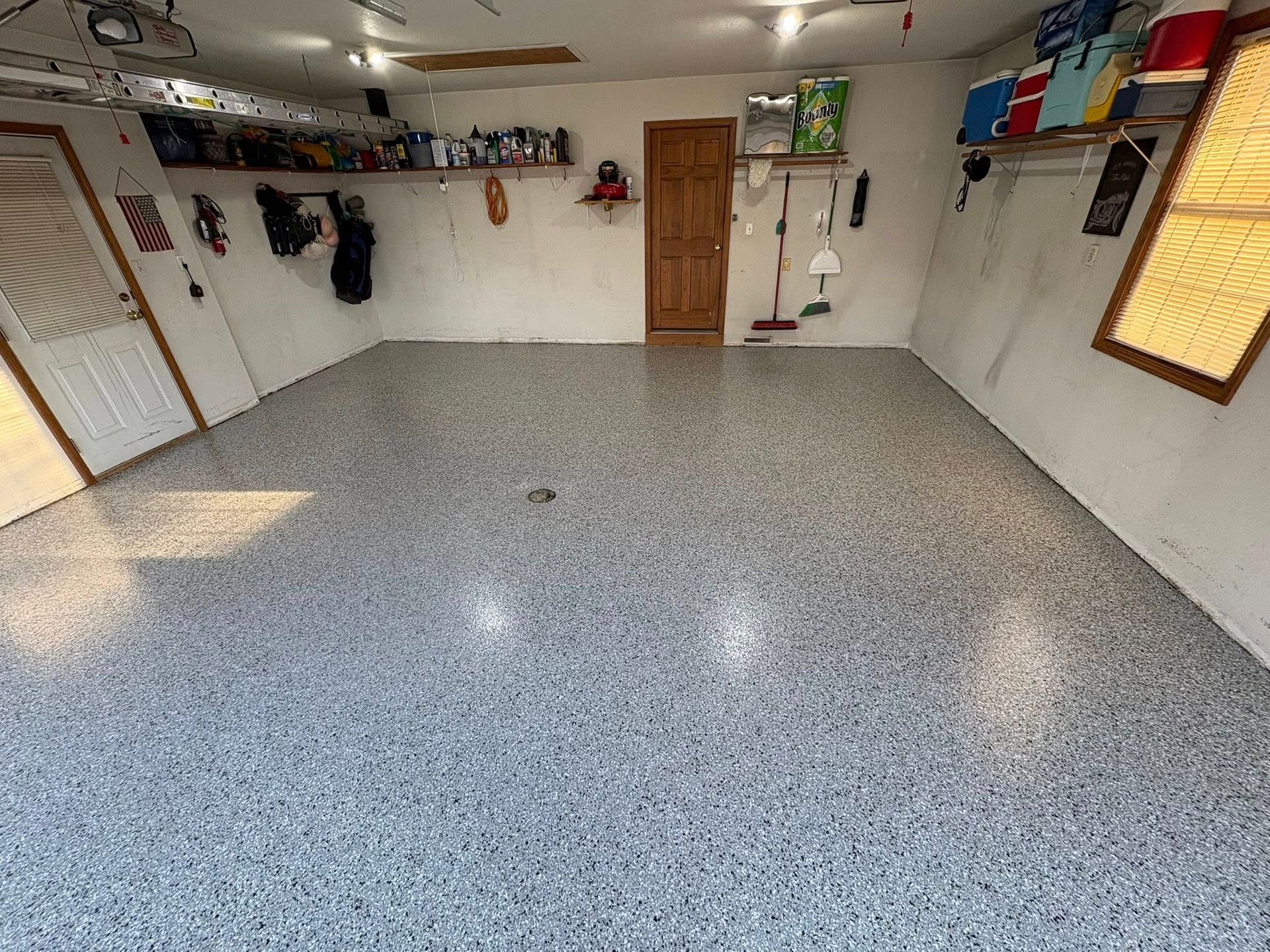 Empty garage with gray speckled floor, white walls, storage shelves, and a wooden door.