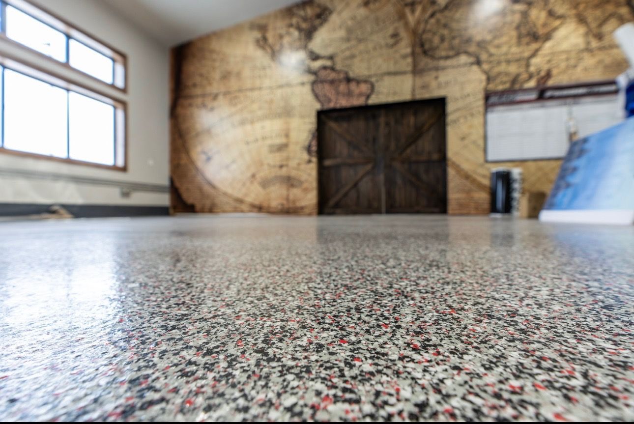 Speckled floor in an empty room with a mural wall, large wooden doors, and a window