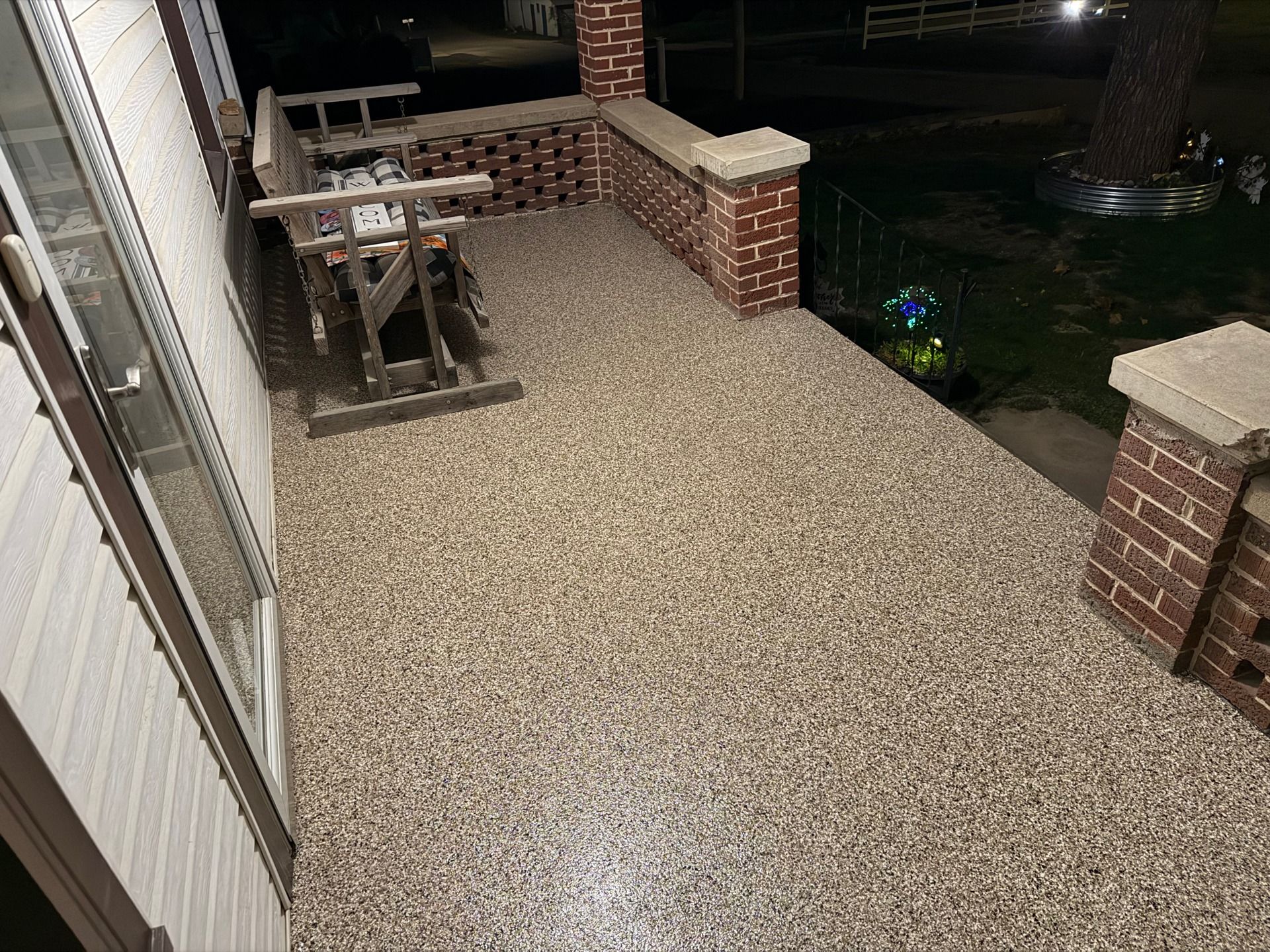 Gravel patio beside a house with a brick ledge, picnic table, and yard at night