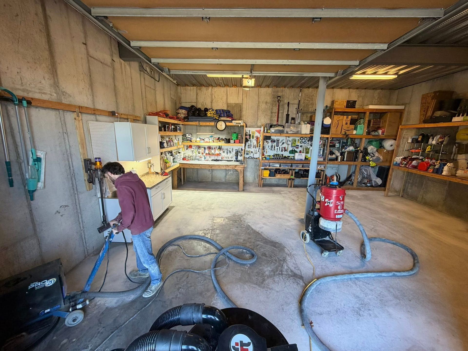 Garage workshop with a person using a vacuum and another cleaning supplies on shelves