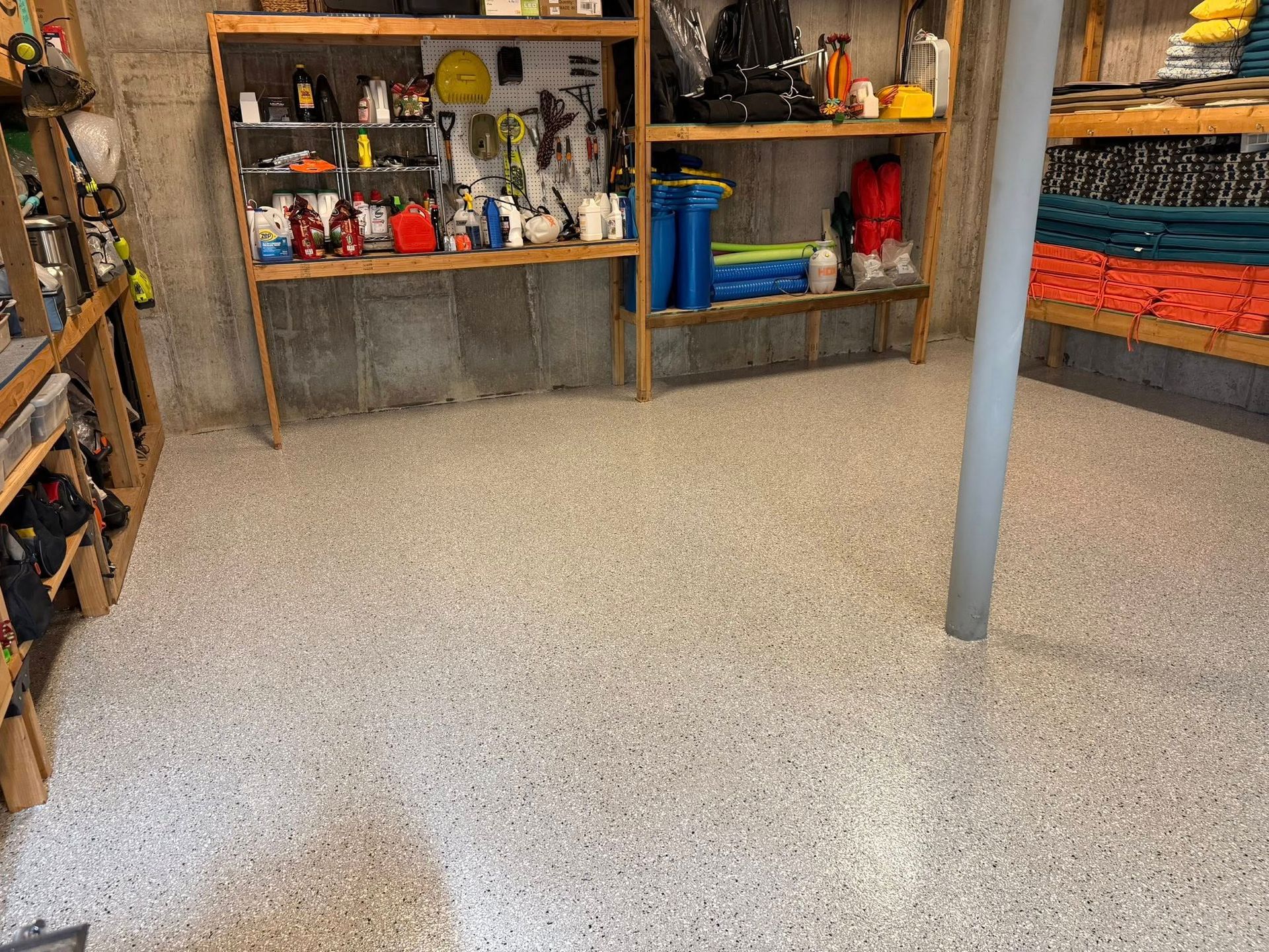 A cluttered workshop with shelves of tools and supplies over a speckled floor.
