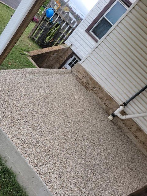 Gravel patio beside a house, with a small concrete ramp and a fenced yard beyond.