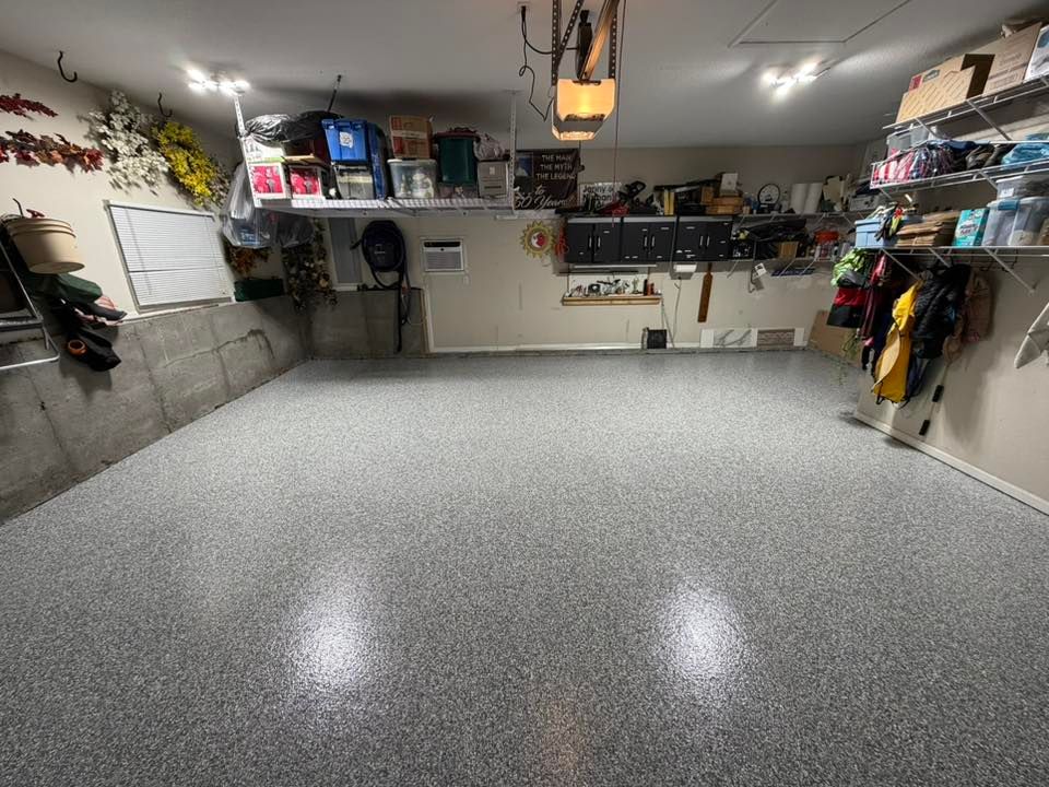 Wide garage with speckled epoxy floor, wall-mounted shelves, and storage boxes along the sides.