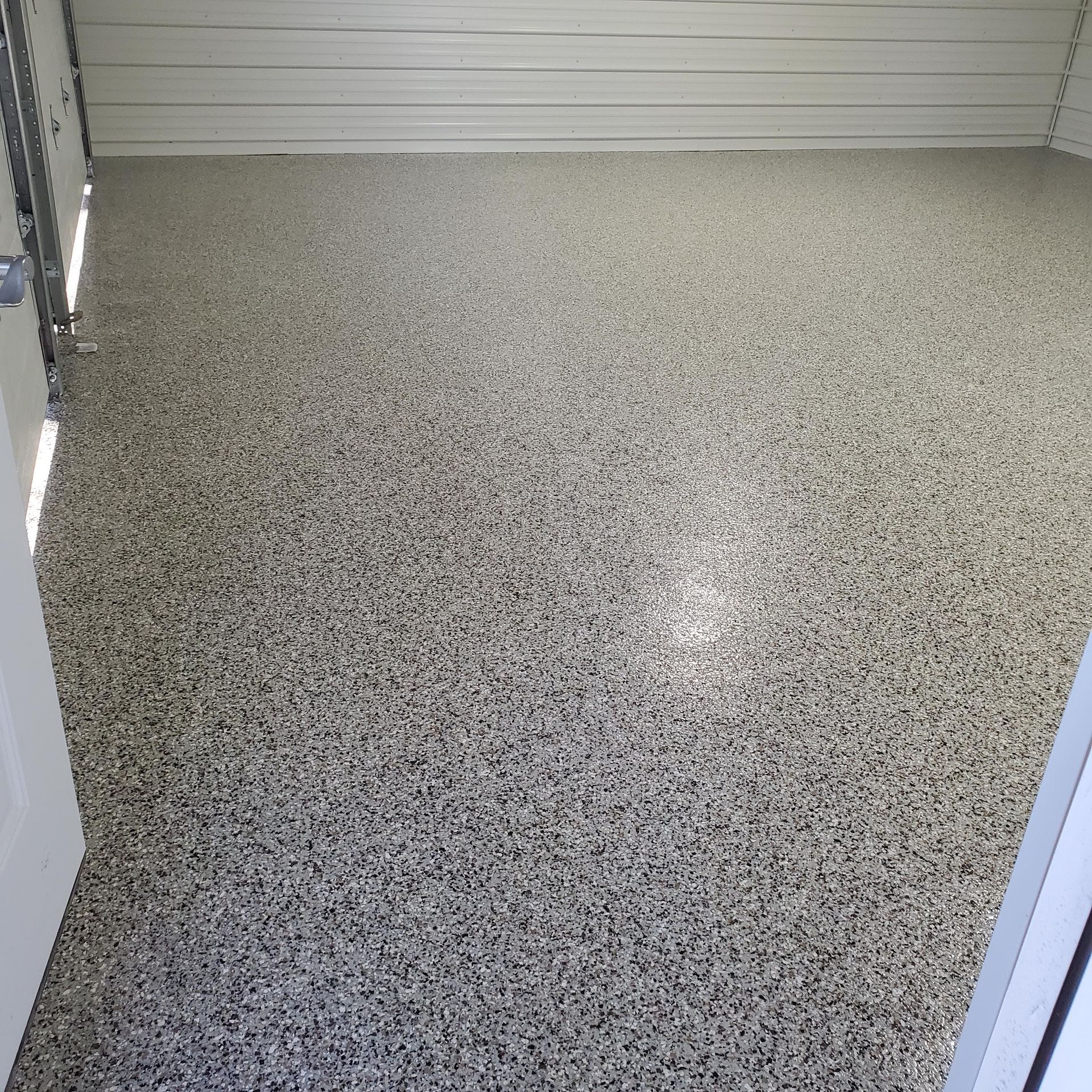 Empty speckled gray garage floor with a white roll-up door in the background
