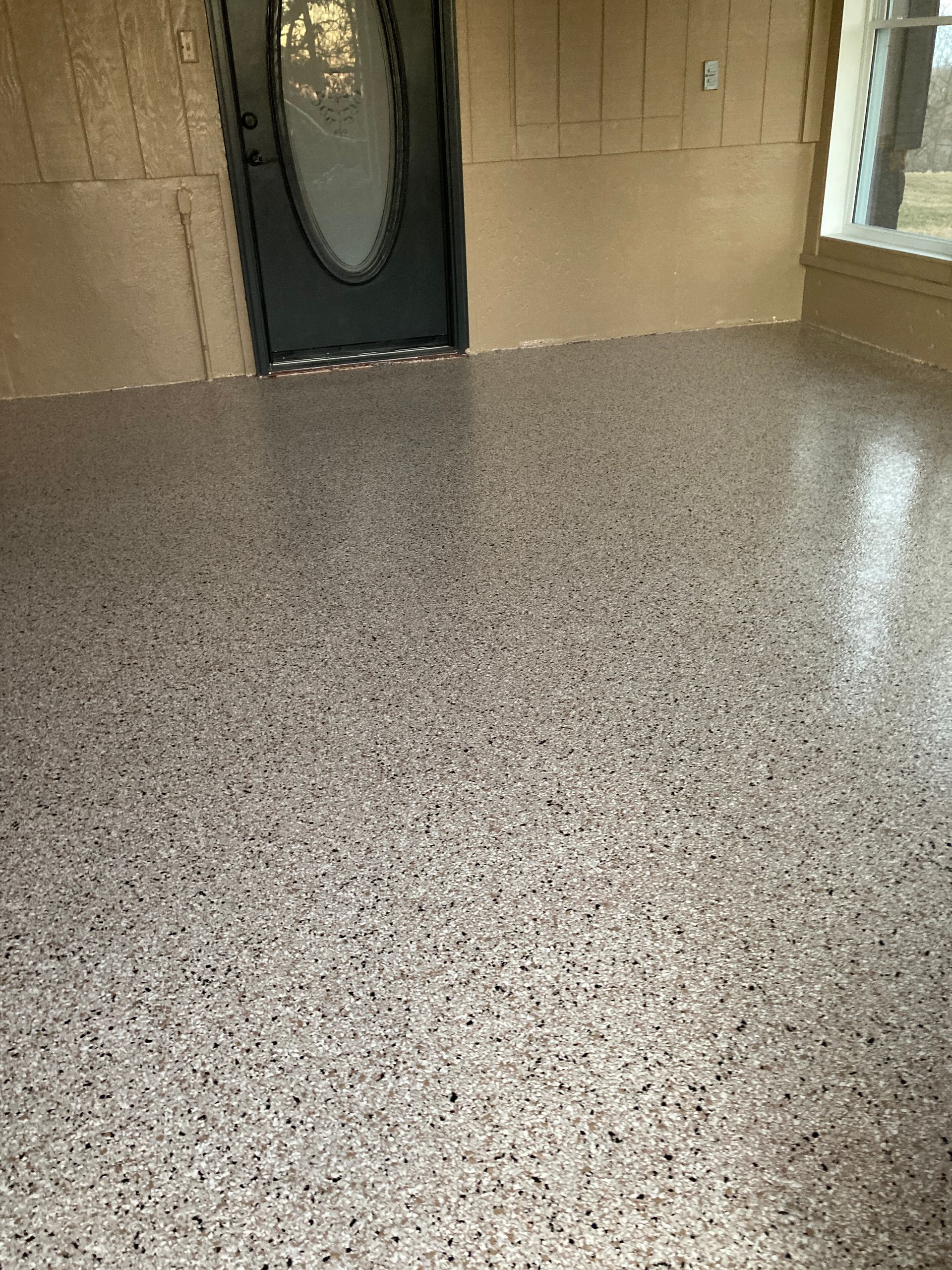 Speckled epoxy floor in a small entryway with a dark front door and windows on the right.