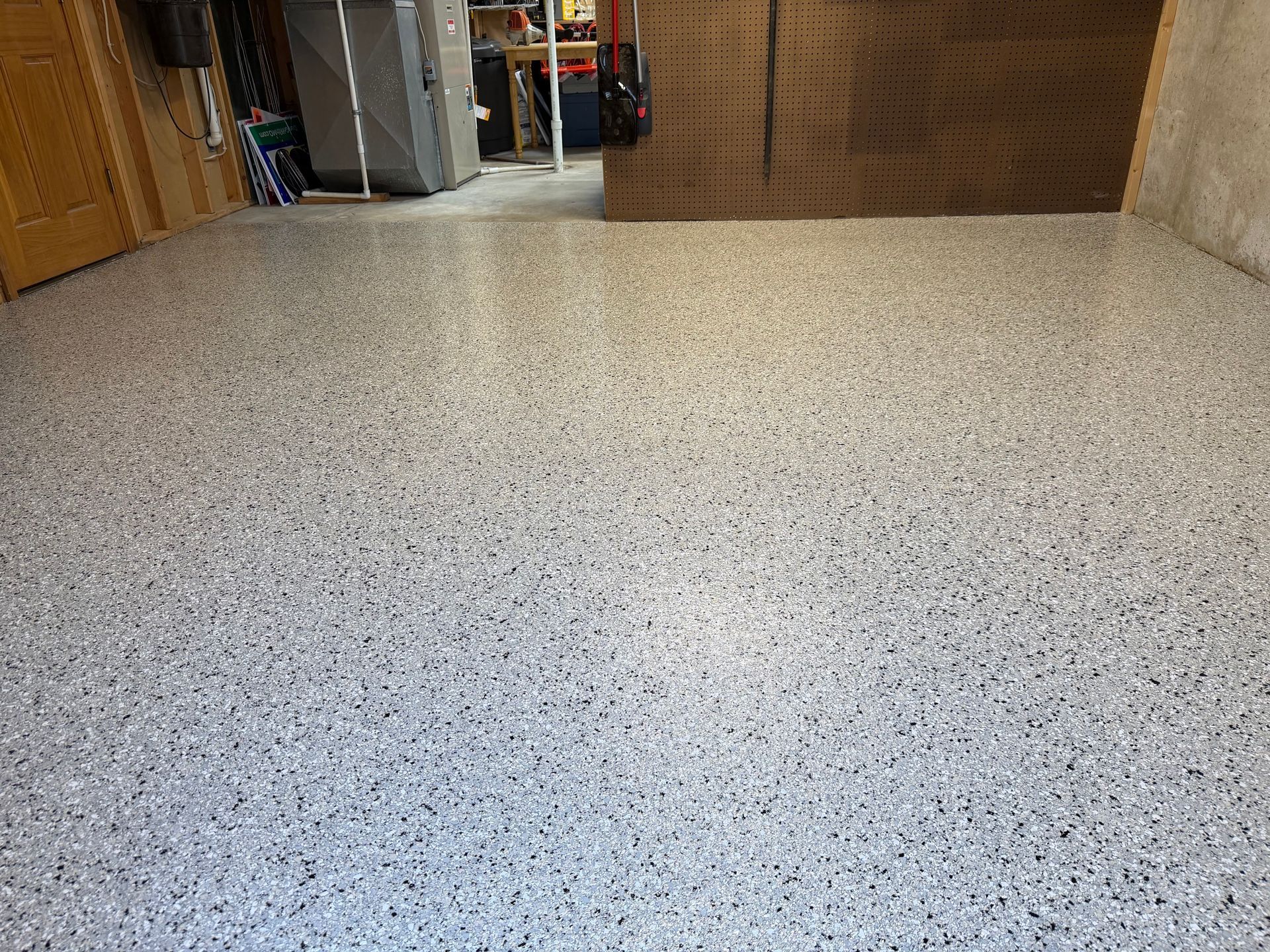 Speckled light-gray floor in a room with wooden walls and an open doorway in the background
