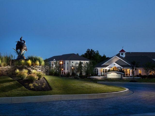 Luxury home at dusk with lit windows, landscaped lawn, and a horse statue on a hill near the driveway at Apartments at Charlestown Crossing.